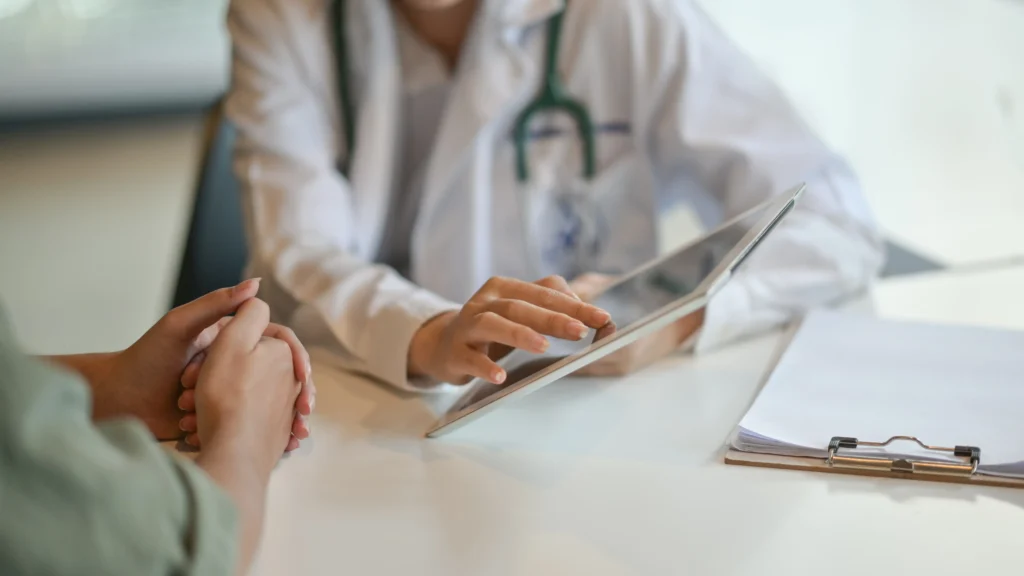 Médica apontando para a tela de um tablet durante consulta sobre dor nas costas com um paciente.