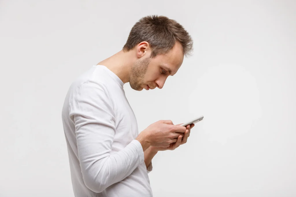 Homem inclinado mexendo no celular, posição que exige cuidados com a reeducação postural.